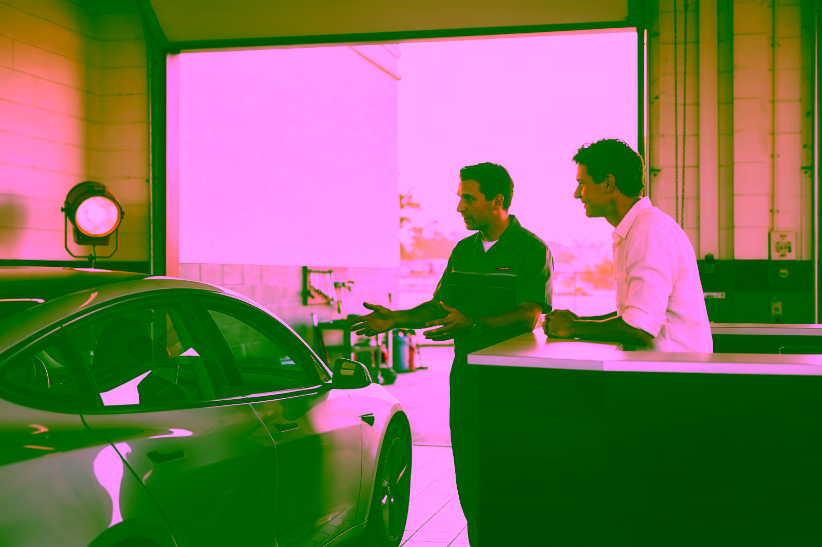 Un asesor y un cliente conversan junto a un automóvil plateado en un taller.
